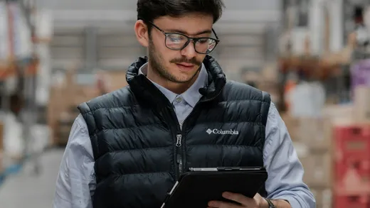 Trabajador de bodega consultando un dispositivo entre estanterías de almacén